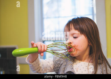 Girl licking chocolate cake mix  off a whisk Stock Photo