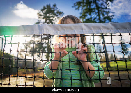Girl hiding behind tennis net laughing Stock Photo