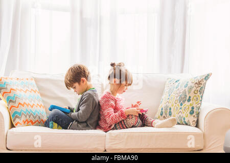 Boy and girl sitting back to back using digital tablets Stock Photo