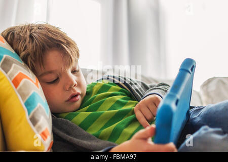 Boy lying on couch playing with digital tablet Stock Photo