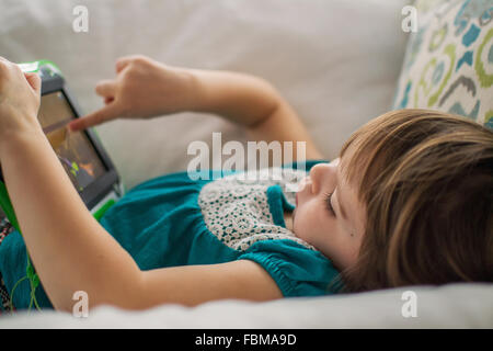 Girl  lying on couch playing with digital tablet Stock Photo