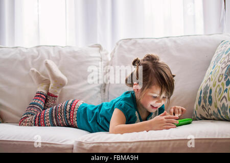 Girl lying on couch playing with digital tablet Stock Photo