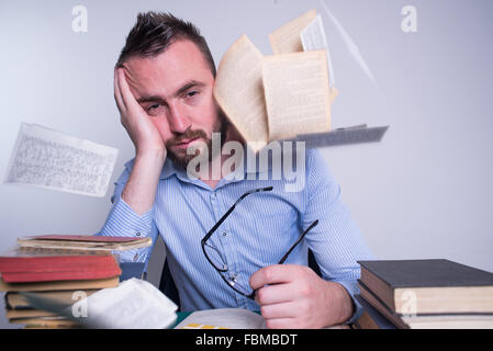 Frustrated man resting head in hand with books and papers flying around Stock Photo
