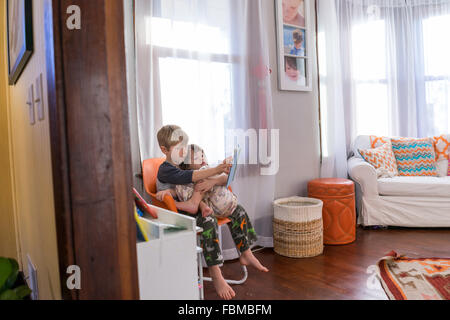 Boy sitting sister on his lap reading a book Stock Photo