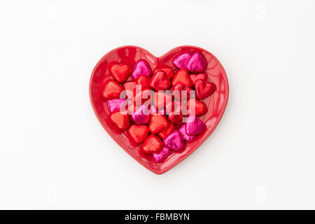 A red, heart shaped Valentine's Day plate full of chocolates on an isolated white background. Stock Photo