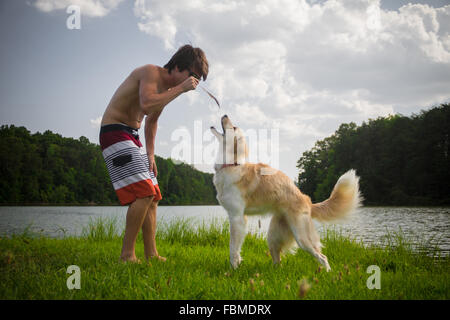 Young man playing with a border collie dog by lake Stock Photo