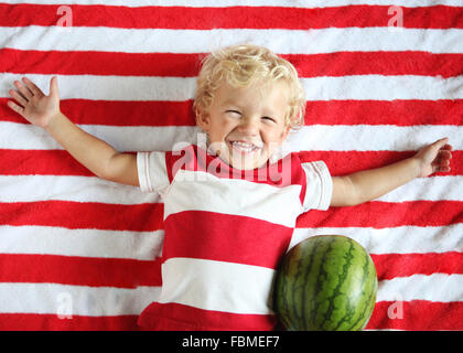 Smiling boy lying on stripy blanket with watermelon Stock Photo