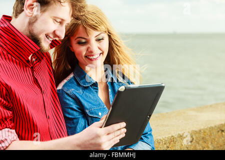 Modern technology devices and tourism concept. Young couple outdoor against sea water with tablet enjoying summer holidays Stock Photo