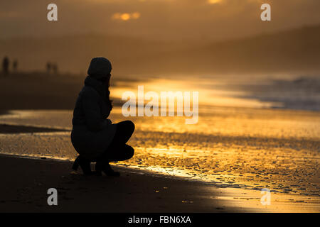 The silhouette of a caucasian young woman by sunset in Valdearenas Beach, Liencres, Pielagos. Cantabria, Spain. Stock Photo