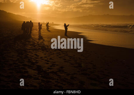 Some people's silhouettes by sunset in Valdearenas Beach, Liencres, Pielagos. Cantabria, Spain. Stock Photo