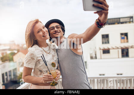 Couple of friends having a party on the rooftop taking a selfie with woman drinking cocktail. They are happy and joyful. Stock Photo