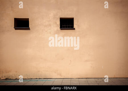 Aged weathered brown street wall with two small windows Stock Photo