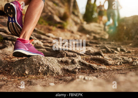 Close up of an athlete's feet wearing sports shoes on a challenging dirt track. Trail running workout on rocky terrain outdoors. Stock Photo