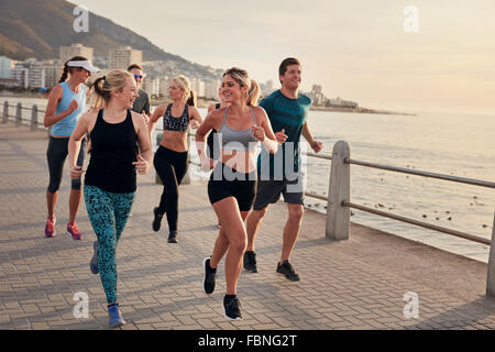 Portrait of young runners enjoying workout on the sea front path along the shoreline.  Running club group running along a seasid Stock Photo