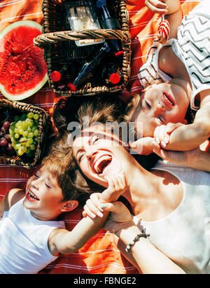 cute happy family on picnic laying on green grass mother and kids, warm summer vacations close up, brother and sister Stock Photo