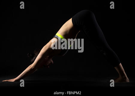 Portrait of sporty beautiful young brunette woman in sportswear bra and black pants working out, doing downward-facing dog pose Stock Photo