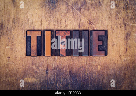 The word "Tithe" written in dirty vintage letterpress type on a aged wooden background. Stock Photo