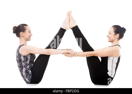 Smiling sporty yogi twin sisters doing fitness training, yoga asana in pair Ubhaya Padangusthasana (Both Feet Big Toe Posture) Stock Photo