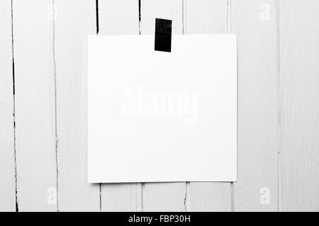 Blank white poster hanging on a tape on white wooden plank wall. Stock Photo