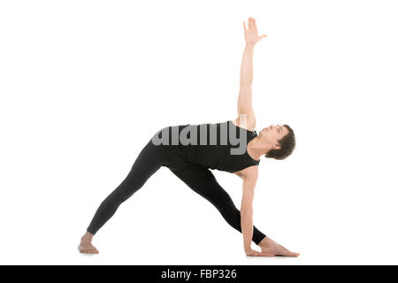 Sporty young man practicing yoga, doing stretching exercise, extended triangle pose, utthita trikonasana asana for flexible Stock Photo