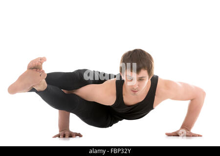 Sporty young man doing yoga or pilates arm balancing exercises, asana Astavakrasana, asymmetrical arm balance, Eight-Angle Pose Stock Photo