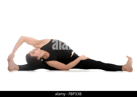 Athletic young man doing yoga, pilates, stretching practice, sitting in splits, Parivrtta Upavistha Konasana, Revolved Seated Stock Photo