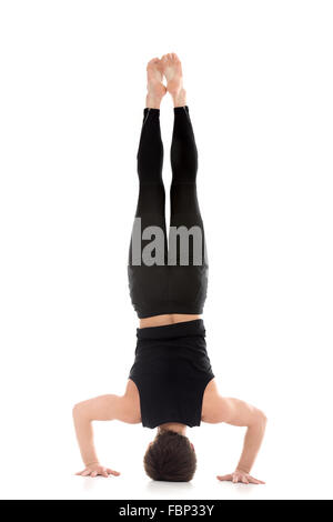Sporty young man working out, yoga, pilates, fitness training, doing Tripod Headstand, Salamba Sirsasana II, back view Stock Photo