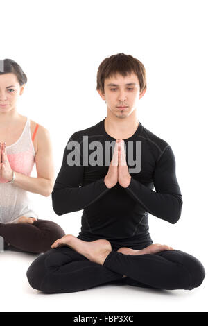 Portrait of two sporty people practicing yoga, couple training together, friends sitting with hands in Namaste gesture in lotus Stock Photo