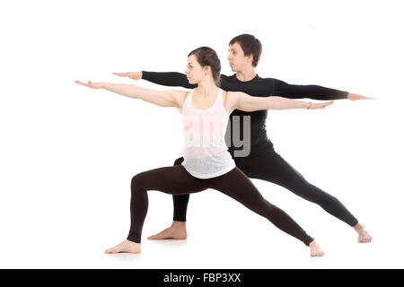 Two sporty people practice yoga with partner, doing lunge exercise, Warrior II posture, Virabhadrasana 2, side view Stock Photo