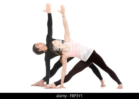 Two sporty people practice yoga with partner, couple doing stretching exercise, extended triangle pose, utthita trikonasana Stock Photo