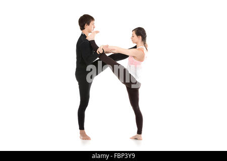 Two sporty people practice yoga in pair, fit couple doing acroyoga, stretching exercise, Extended Hand to Big Toe yoga pose Stock Photo