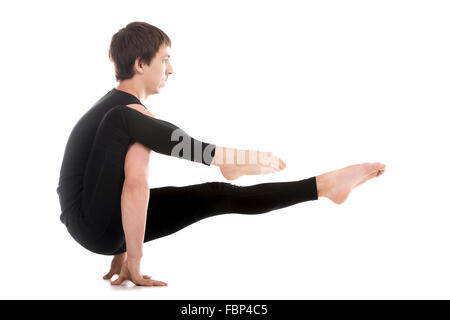 Sporty attractive young man working out, doing handstand exercises, Eka Hasta Bhujasana Elephant Trunk or Leg over shoulder Pose Stock Photo