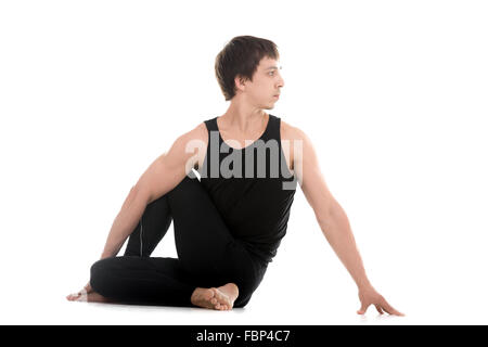 Sporty attractive young man working out, siting in Half lord of the fishes pose, Ardha Matsyendrasana, therapeutic for digestive Stock Photo