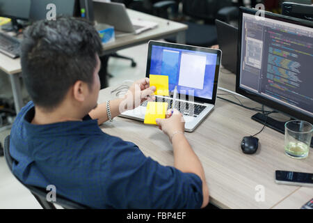 Asian business man yellow sticky note, rear back view thinking idea computer developer working desk laptop Stock Photo