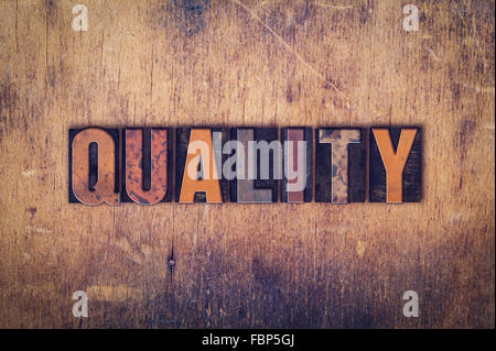 The word "Quality" written in dirty vintage letterpress type on a aged wooden background. Stock Photo