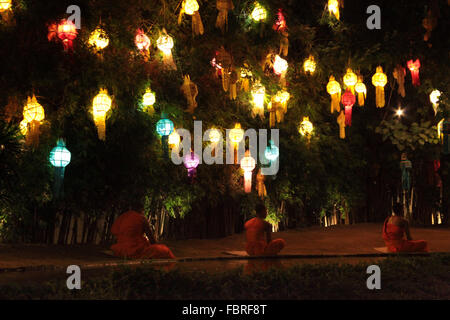Chiang Mai, Thailand, 2016. Monks in saffron robes sitting under tree lit with hundreds of lanterns in prayer. Stock Photo