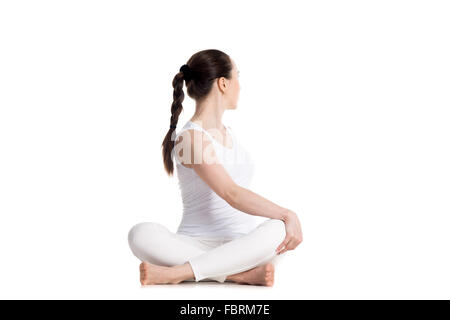 Sporty beautiful young woman in white sportswear practicing yoga, sitting cross legged in Revolved easy pose, spinal twist Stock Photo