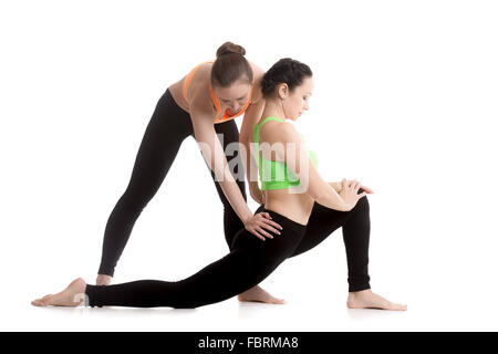 Two beautiful sporty girls practice yoga with partner, coach helps student to build correct posture, stretching, asana Ardha Stock Photo