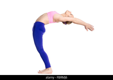 Sporty beautiful young blond woman in purple leggings doing Standing Backward Bend yoga posture, Half Wheel pose, studio Stock Photo