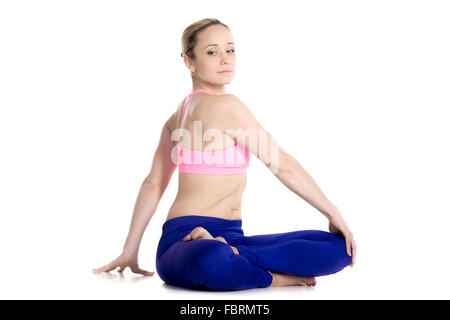 Sporty beautiful blond young woman sitting in variation of Lotus pose, parivrtta Ardha Padmasana, Revolved half lotus posture Stock Photo