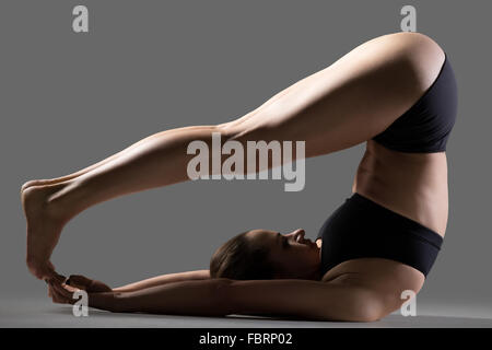 Beautiful young fit woman in sportswear shorts doing sport exercises, variation of Halasana, Plough (Plow) posture, Yin Yoga Stock Photo