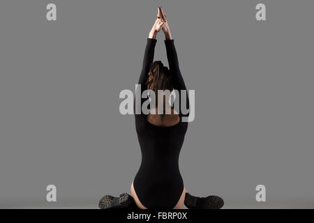 Cool attractive slim young woman doing sports training, stretching exercises, warming up, sitting in variation of Gomukhasana Stock Photo