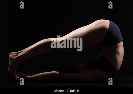 Beautiful young fit woman in sportswear shorts doing sport exercises, Halasana, Plough (Plow) posture, Yin Yoga Snail Pose Stock Photo