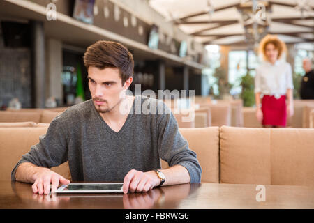 Portrait of a pensive man sitting at the table with tablet computer in restaurant Stock Photo