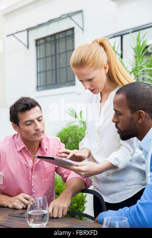 Business team members gathered around collegue presenting idea using digital tablet Stock Photo