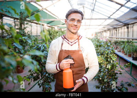 Portrait of attractive male gardener in glasses standing and holding water pulveriser in greenhouse Stock Photo