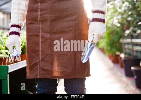 Closeup of garden tools for transplantation plants holded by hands of male gardener in gloves in greenhouse Stock Photo
