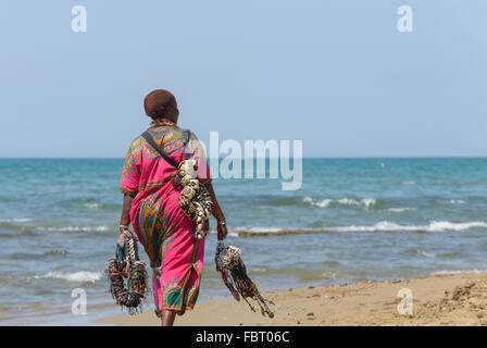 Rome, Italy - August 13, 2015: a black woman walking and selling necklaces and bracelets on the beach Stock Photo