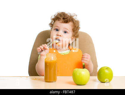 little child eating puree with spoon sitting at table with fruits Stock Photo