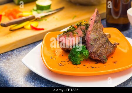 Delicious medium rare sirloin steaks and vegetables placed on orange plate, elegant presentation Stock Photo